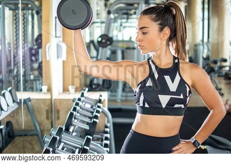 Side View Of Beautiful Attractive Young Fit Sporty Woman Lifting Dumbbell In The Gym.