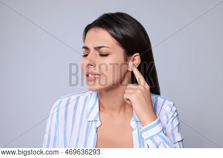 Young Woman Suffering From Ear Pain On Light Grey Background