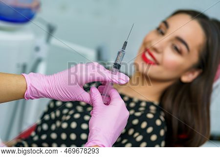 Dentist Holding A Syringe For Anesthetizing Patient. Dental Concept. Smiting Patient On Blurred Back