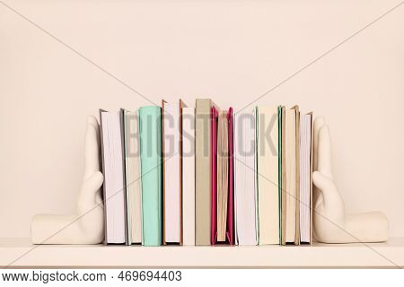Beautiful Hand Shaped Bookends With Books On Shelf Near Beige Wall