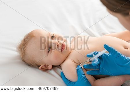 Doctor Vaccinating Smiling Baby In Clinic. One Year Little Baby Get An Injection. Pediatrician And P