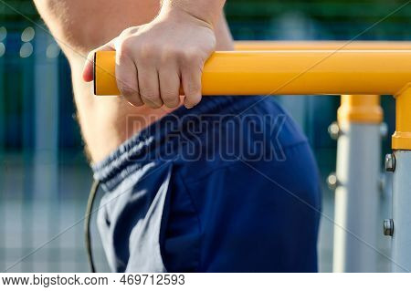 Close-up Of A Man In Sports Shorts Doing Push-ups On Parallel Bars At An Outdoor Stadium. A Strong Y