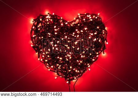 Shape Of Heart Folded From Tangled Wires Of A Garland With Red Light Bulbs On Red Background In The 