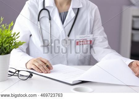 A Doctor In A White Coat With A Pharyngoscope Sits In A Medical Office, Fills Out Paperwork And Look