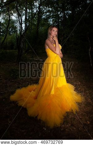A Fragile, Tender Girl In A Yellow Vintage Dress Laying Down On A Fallen Tree . Background Of A Myst
