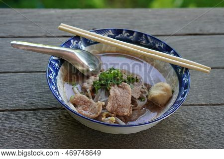Hot Noodles With Meatballs And Nam Tok Pork Put In A Ceramic Bowl, Chopsticks And Spoon, On Wooden F
