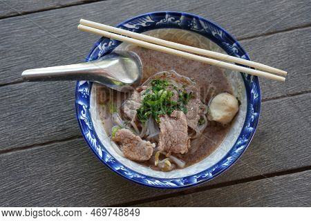 Top View Noodles With Meatballs And Nam Tok Pork Put In A Ceramic Bowl, Chopsticks And Spoon, On Woo