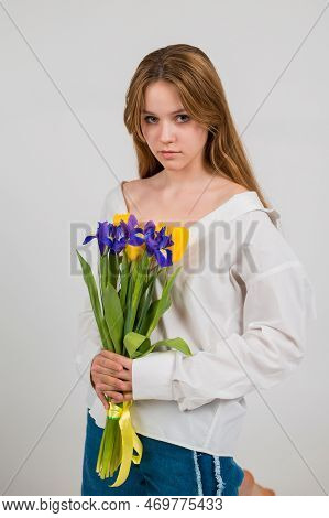 A Blonde Girl In A White Shirt And Blue Jeans Holds A Bouquet Of Tulips And Irises Sitting On A Whit