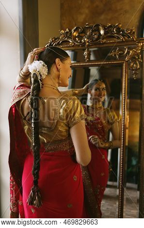 Female Model Hindu Bride In Saree, Wearing Gold And Jasmine Flower Garlands In The Hair Near Mirror