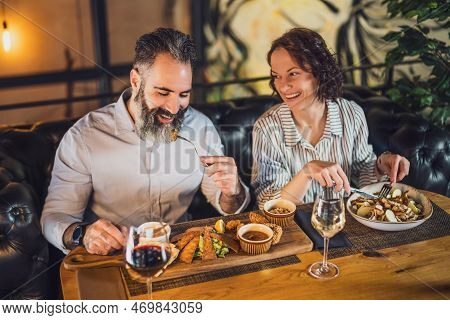 Happy Couple Is Sitting At Restaurant. They Are Having Dinner With Wine And Spending Nice Time Toget