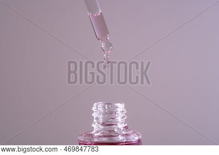 Pink Face Oil Drop From Glass Pipette Dropper. Macro Close Up For Cosmetic Neutral Background Bakuch