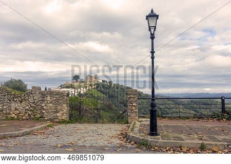 Photo Of Picturesque Street With Street Lamp. Iron Gate With View Of Medieval Castle On Hill.