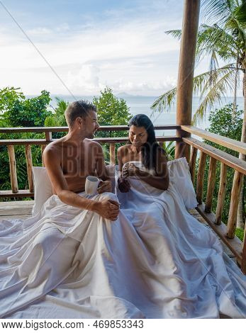 Couple Waking Up In Bed Looking Out Over Ocean During Sunrise At Wooden Hut Moutains Of Thailand