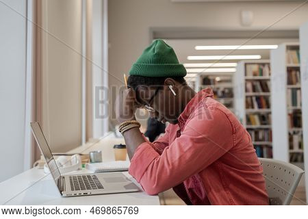 Tired Apathetic African American Man Sits At Table With Laptop With Eyes Closed Due To Overwork Prep