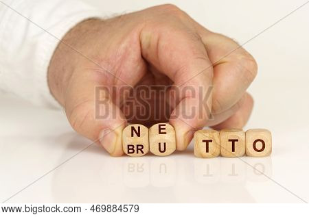On A Reflective White Surface In The Hands Of A Man Are Cubes With The Inscription - Netto Or Brutto
