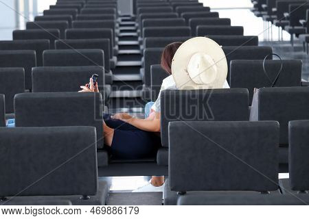Passengers Are Waiting For Their Flight In Airport Terminal. Couple Sitting With Smartphone In Empty