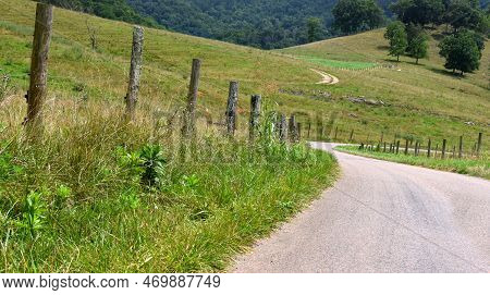 Curving, Country Road Winds Between Fenced In Pasture In The Appalachian Mountains.  Rustic Fence Po