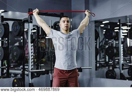 A Muscular Sportsman Doing Fitness Exercises With Resistance Band In A Gym.