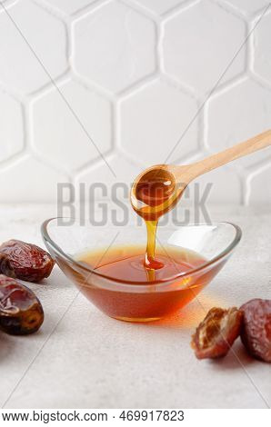 Natural Organic Healthy Date Syrup Flows From Wood Spoon Into A Glass Bowl With Whole Dates On The B