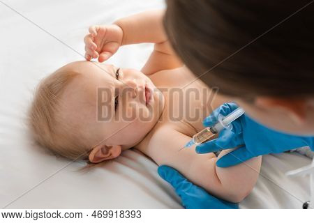 Doctor Vaccinating Smiling Baby In Clinic. One Year Little Baby Get An Injection. Pediatrician And P