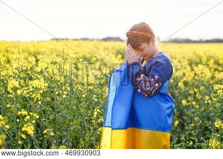 Pray For Ukraine. Child With Ukrainian Flag In Rapeseed Field. Girl Holding National Flag Praying Fo