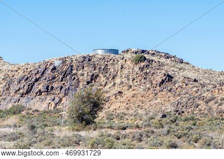 A Landscape, With The Remnants Of A Windmill And A Corrugated Iron Dam On A Hill On The Road Between