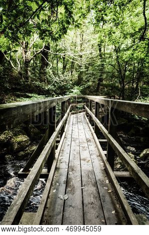 A Wooden Bridge Over A River In A Woodland Gorge.