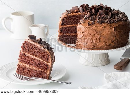 A Piece Of Homemade Chocolate Cake With The Rest Of The Cake In Behind.