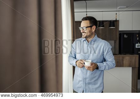 A Smiling Man Looks Trough The Window While Holding Fresh Morning Coffee.