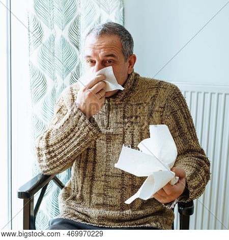 Middle-aged Man In Warm Sweater, Blows Nose Into Disposable Paper Napkin, Sneezes And Coughs, Is Sic