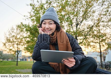 Portrait Of Asian Girl Relaxing In Park, Watching Videos Or Reading On Digital Tablet, Sitting On Be