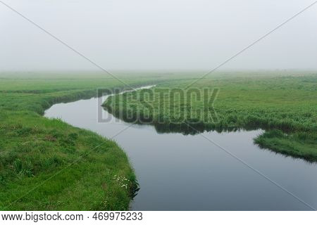 Morning Landscape, A Vast Meadow With Calm River Among Lush Grass Is Hidden By Fog