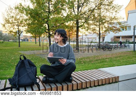 Young Girl, Korean Artist Or Art Student Sits In Park With Digital Tablet, Draws With Graphic Pen, S