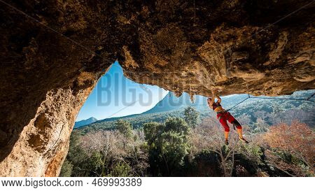 A Young Rock Climber On An Overhanging Cliff. The Climber Climbs The Rock. The Girl Is Engaged In Sp