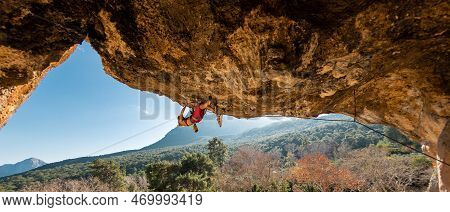 A Young Rock Climber On An Overhanging Cliff. The Climber Climbs The Rock. The Girl Is Engaged In Sp