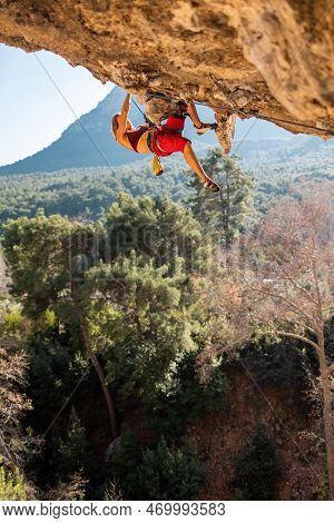 Girl Climber On An Overhanging Rock. A Sports Woman Climbs A Rock Against The Backdrop Of Mountains.