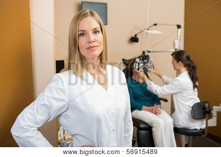 Portrait of female eyecare specialist with colleague examining patient in background