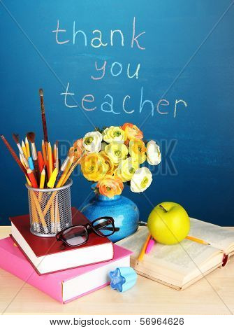 School supplies and flowers on blackboard background with inscription Thank you teacher