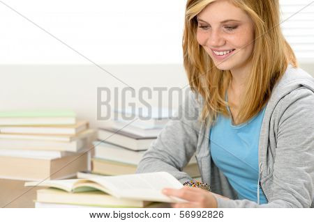 Smiling student girl reading book looking down sitting behind desk