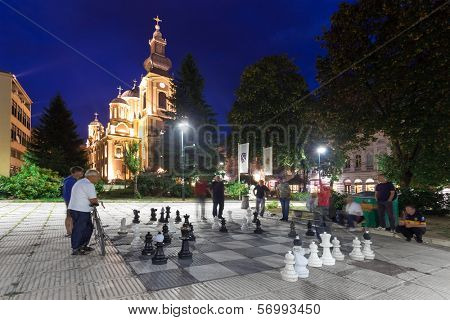 SARAJEVO, BOSNIA AND HERZEGOVINA - AUGUST 13, 2012: Men play chess on the street with large chess pieces at night with church in background.