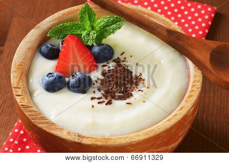 natural samolina pudding with fresh blueberries and strawberries, sprinkled with grated chocolate and served in the ceramic bowl with wooden spoon