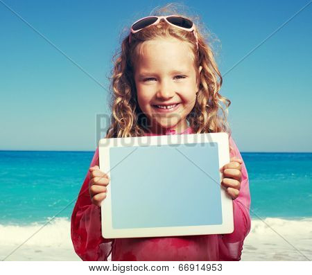 Child on the beach with tablet computer. Little happy girl showing screen digital pc
