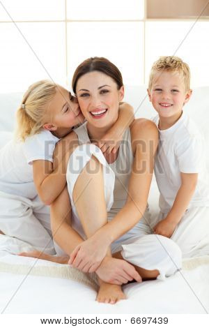 Crianças cute beijando sua mãe sentada em uma cama