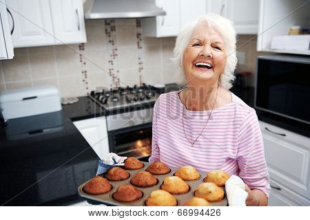A laughing pensioner holding a tray of baked muffins just out of the oven