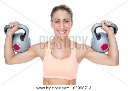 Happy female crossfitter lifting kettlebells looking at camera on white background