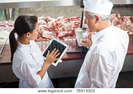 Side view of male and female butchers using digital tablet in store