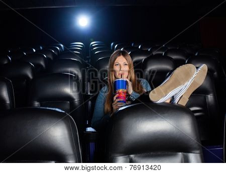 Woman with feetup on seat drinking cola while watching movie at cinema theater