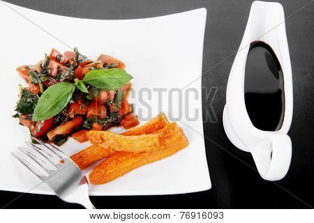 vegetable salad : cherry tomatoes and basil with sweet baked potato served on white plate with sauceboat full blask soy sauce on wood