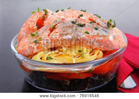 fresh fried natural pink salmon on italian traditional tagliatelle backed with tomato and vegetables served over black wooden table