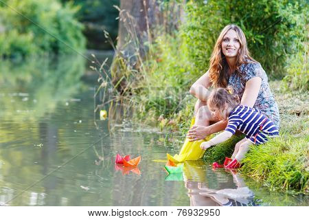 Adorable Little Girl And Her Mom Playing With Paper Boats In A River.